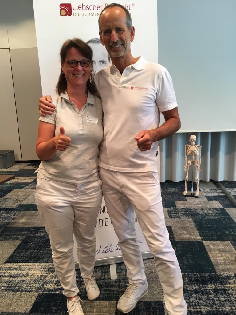 Auf dem Foto steht Petra Fietze-Jank neben Roland Liebscher-Bracht. Beide halten einen Daumen nach oben und tragen weiße Kleidung. Petra Fietze-Jank hat schulterlange braune Haare und einen geraden Pony sowie eine eckige dunkle Brille.