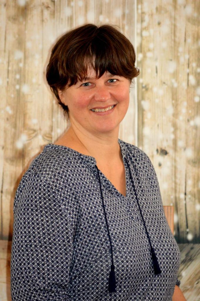 Das Foto zeigt Katrin Hartmann aus Beetzsee vor einem erleuchteten hellen braunen Hintergrund. Sie hat kurze braune Haare und trägt eine blau-weiße Bluse an.